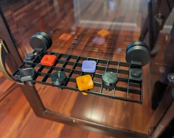 May include: A black, grid-like shelf with various colorful, geometric shapes and black circular attachments. The shelf is mounted on a glass surface, with a wooden table visible in the background. The shapes include red, orange, and purple squares.