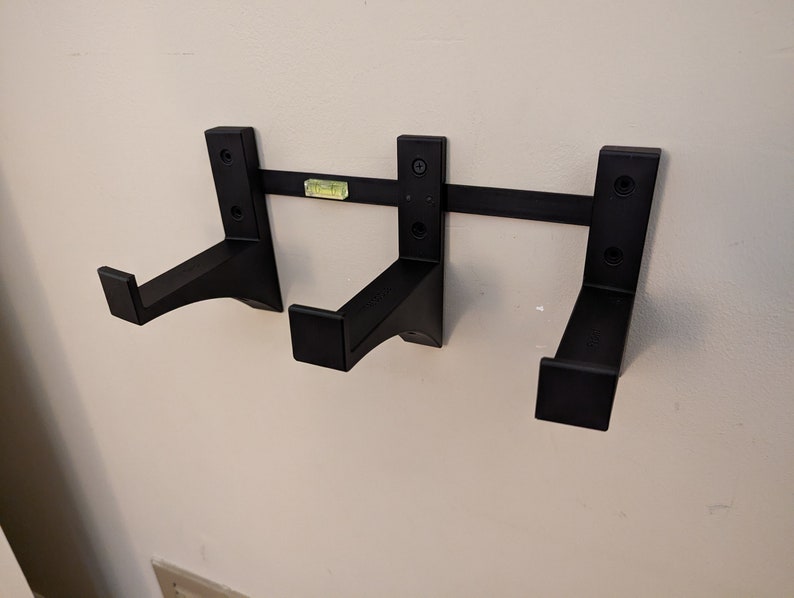 May include: Three black wall-mounted brackets with a horizontal bar connecting them. The brackets have a curved design and are ideal for hanging items.