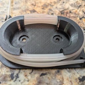 May include: A black plastic spool holder with a white cord wrapped around it. The holder has two holes on the top.