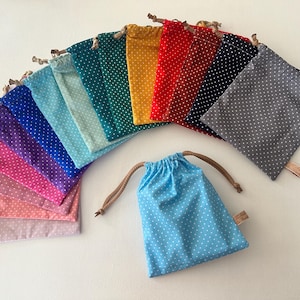 Peut inclure: Une collection de petites pochettes en tissu à cordon de serrage disposées en éventail. Chaque pochette présente un motif à pois blancs sur un fond de couleur unie, incluant des tons de bleu, vert, jaune, rouge, violet, rose et gris avec des cordons.