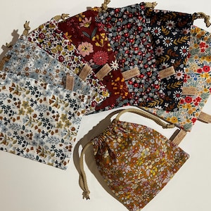 Peut inclure: Un ensemble de neuf petits sacs en tissu avec des motifs floraux. Les sacs sont en coton et ont une fermeture à cordon. Les sacs sont de couleurs et de motifs différents, notamment rouge, bleu, vert et jaune.