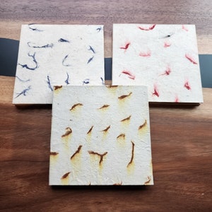 May include: Three handmade paper squares with different patterns. The first square has blue ink splatter, the second has red ink splatter, and the third has brown ink splatter.