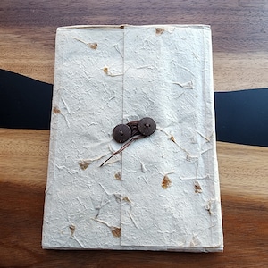 May include: A white paper envelope with a textured surface and brown buttons. The envelope is closed with a brown string.
