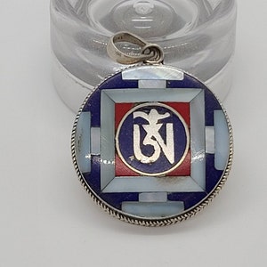 May include: A silver pendant with a blue, red, and white inlay design. The pendant features a Tibetan symbol in the center.