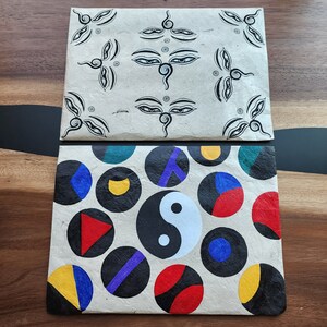 May include: Two rectangular paper envelopes with a decorative design. The top envelope has a black and white design of stylized eyes. The bottom envelope has a black and white design of circles with different colors and patterns.
