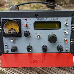 Puede incluir: Un transceptor Penntek TR-45 Lite S-Band S-Watt CU de color gris y negro con un botón de encendido rojo y una base roja. El transceptor tiene una variedad de perillas e interruptores, que incluyen un bloqueo de marcación, sintonización, muesca, volumen y encendido.