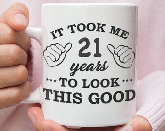 May include: White ceramic coffee mug with black text that reads "It took me 21 years to look this good".