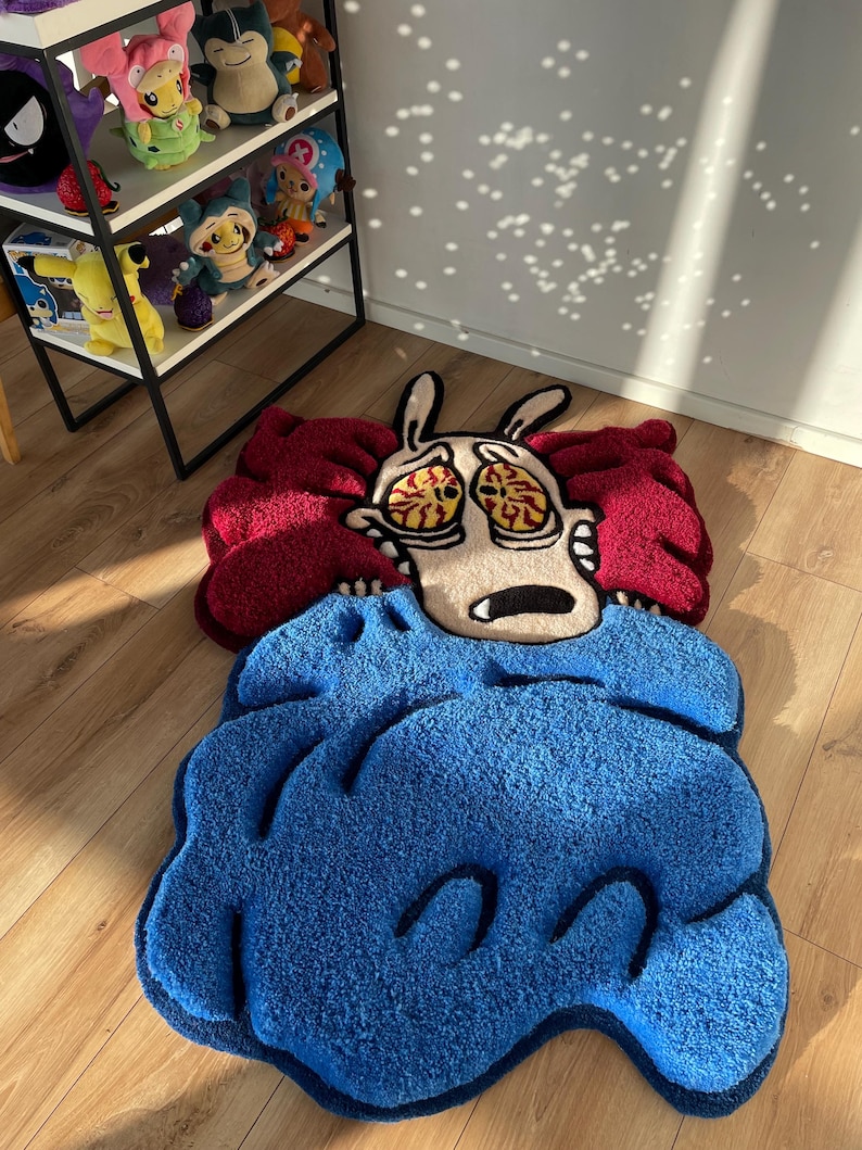 May include: A blue and red rug with a cartoon character of a dog with big eyes and a worried expression. The dog is under a blue blanket and has a red and white head.