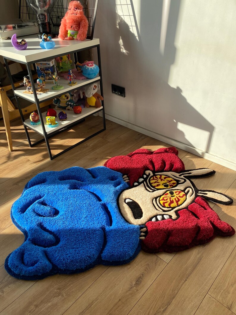 May include: A blue and red cartoon rug with a distressed look. The rug features a character with large eyes and a distressed expression. The rug is made of a soft, plush material.