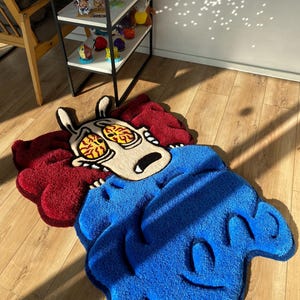 May include: A blue and red rug with a cartoon character design. The character has large eyes and is holding its head. The rug is made of a soft, plush material.