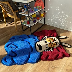 May include: A blue and red rug with a cartoon dog with large eyes and a distressed expression. The rug is made of fluffy material and has a 3D effect.