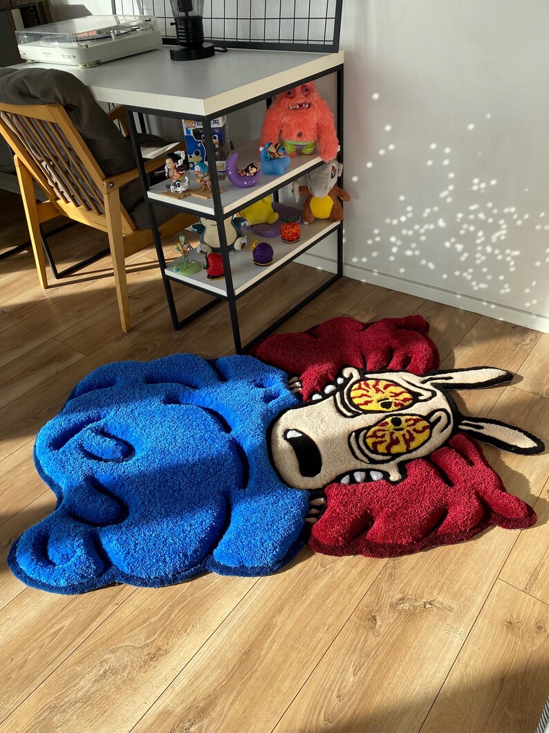 May include: A blue and red rug with a cartoon dog with large eyes and a distressed expression. The rug is made of fluffy material and has a 3D effect.
