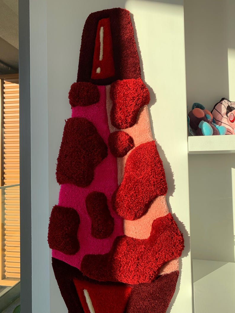 May include: A red, pink, and white abstract rug with a textured, fuzzy surface. The rug is shaped like a tall, narrow bottle.