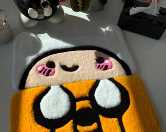 May include: A yellow and white rug featuring a cartoon character design. The character has a yellow body, white eyes, and a black outline. The rug is made of soft, plush material.
