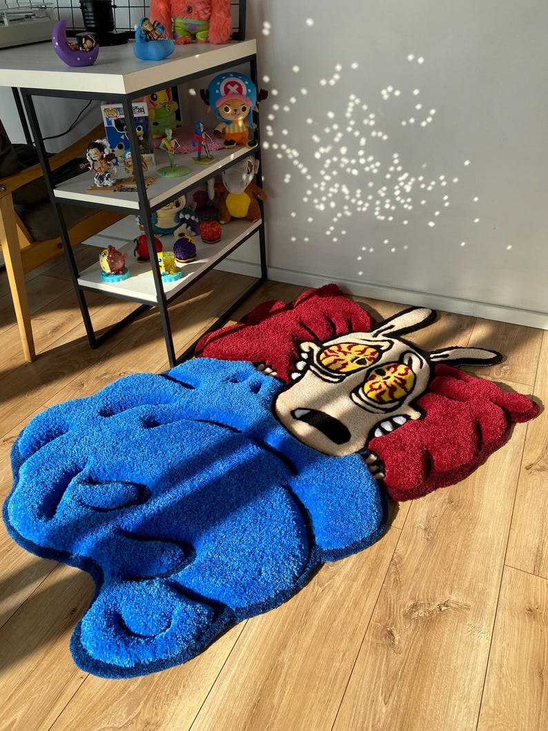 May include: A blue and red cartoon rug with a character with large eyes and a surprised expression. The rug is made of soft, plush material.