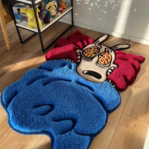 May include: A blue and red cartoon rug featuring a character with large eyes and a red and white striped shirt. The character is lying down on a blue blanket.