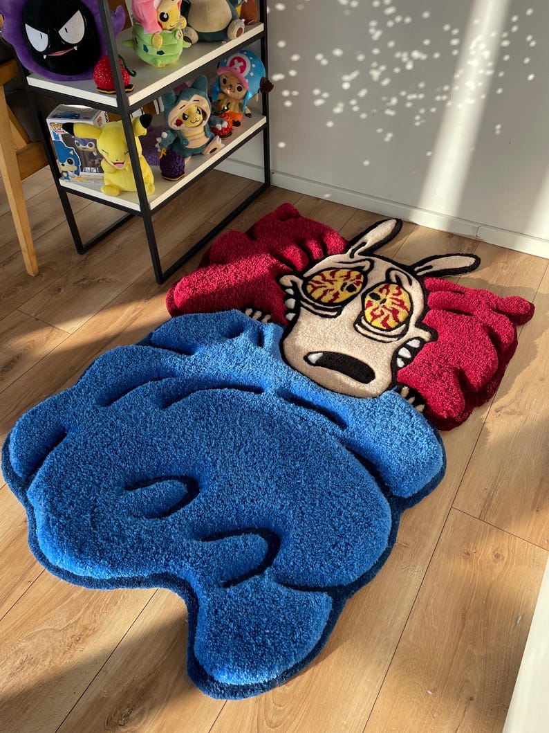 May include: A blue and red cartoon rug featuring a character with large eyes and a red and white striped shirt. The character is lying down on a blue blanket.