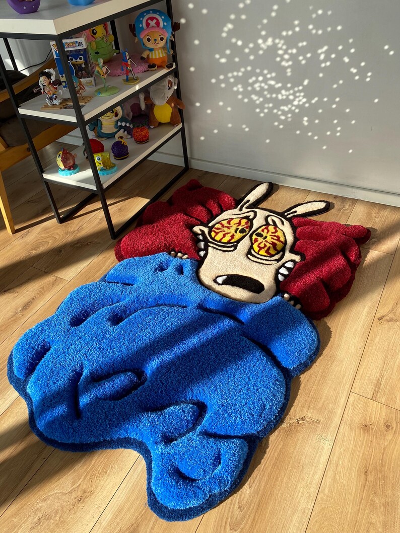 May include: A blue and red rug with a cartoon character of a dog with large eyes and a surprised expression. The rug is made of a soft, plush material.