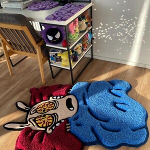May include: A blue and red cartoon rug with a character with large eyes and a surprised expression. The rug is on a wooden floor.