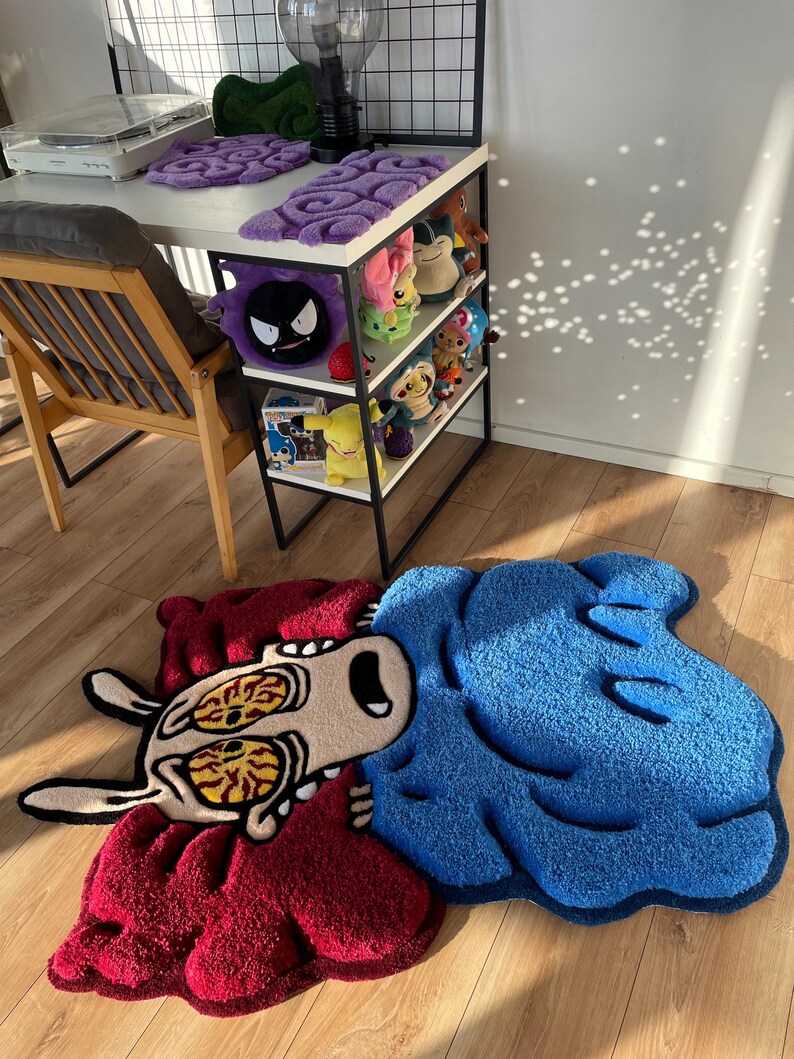 May include: A blue and red cartoon rug with a character with large eyes and a surprised expression. The rug is on a wooden floor.