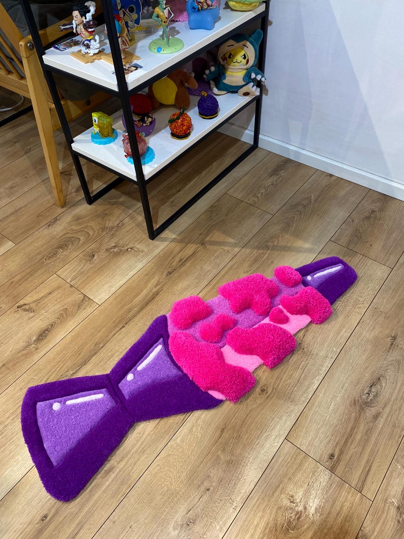 May include: A purple and pink rug shaped like a bottle of soda with a fizzy top. The rug is made of fluffy, textured material.
