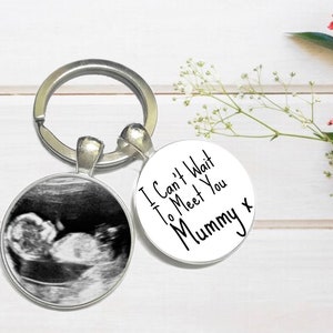 May include: A silver keyring with a round charm featuring a black and white ultrasound image of a baby. The other charm is white with black text that reads "I Can't Wait To Meet You Mummy x".