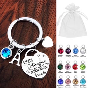 May include: Silver keyring with a heart-shaped charm that reads "Chance made us colleagues but the fun & laughter we share made us friends". The keyring also has a small letter A charm and a blue crystal charm.