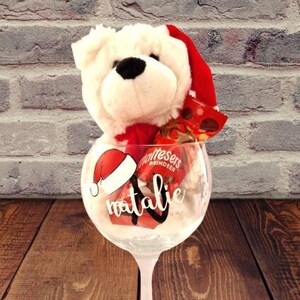 May include: A clear glass with a white Santa hat and the name "Natalie" written on it. The glass is filled with a white teddy bear wearing a red Santa hat and red and white sweets.