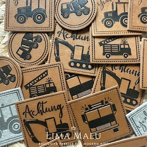 Könnte beinhalten: Eine Sammlung brauner Lederaufnäher mit schwarzen geprägten Illustrationen von Baufahrzeugen, darunter Traktoren, Betonmischer und Bagger. Einige Aufnäher tragen das Wort "Achtung" und den Markennamen "LIMA MALU".