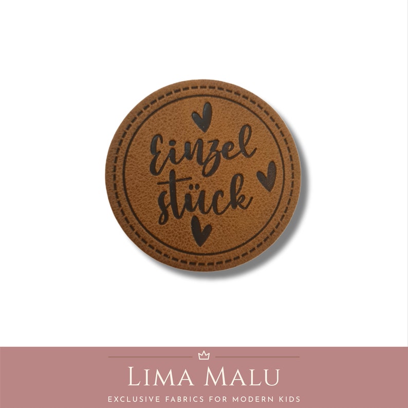 May include: A brown leather patch with a stitched border and the text "Einzelst&uuml;ck" in black lettering. There are three small black hearts around the text.