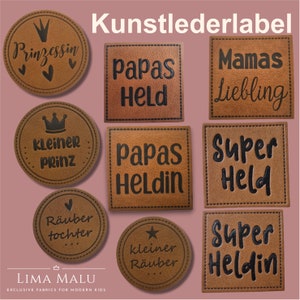 Può includere: Nove etichette in pelle marrone con testo nero. Le etichette presentano varie frasi, tra cui "Papas Held", "Super Held", "Kleiner Prinz" e "Räuber Tochter".