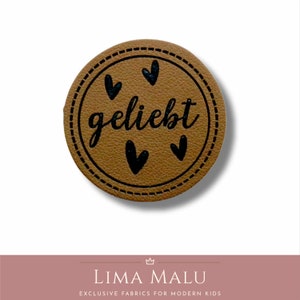 May include: A brown leather label with a stitched border and the word "geliebt" in black script. There are four black hearts around the word.