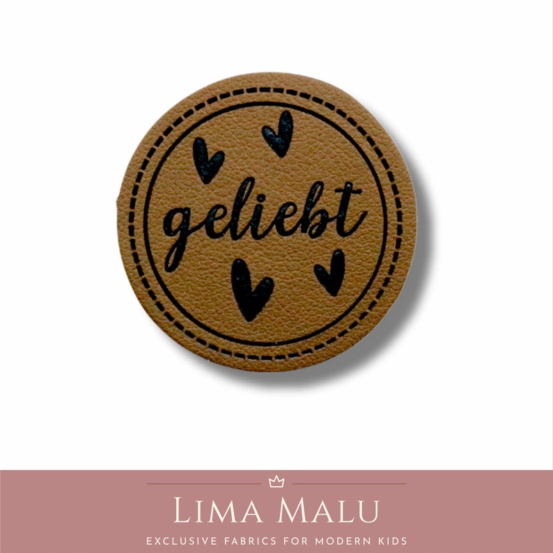 May include: A brown leather label with a stitched border and the word "geliebt" in black script. There are four black hearts around the word.
