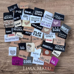 Könnte beinhalten: Eine Sammlung von Stoffetiketten in verschiedenen Farben, jede mit einzigartigem Text und Design. Die Etiketten zeigen Sätze wie "holy shit", "100% Crazy" und "Mommy made". Einige Etiketten haben Herz- und Smiley-Grafiken. Der Markenname "LIMA MALU" steht unten.