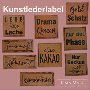 Può includere: Una collezione di etichette in similpelle marrone con vari disegni di testo nero. Le etichette includono frasi come "Drama Queen", "Gold Schatz" e "Ciao Kakao". Le etichette sono cucite sui bordi e sono per bambini moderni.