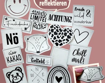 May include: A selection of white fabric patches with black stitched borders and various designs. Includes a smiley face, fox, heart, and text like "ACHTUNG!" and "Chill mal!" The patches are for modern kids.