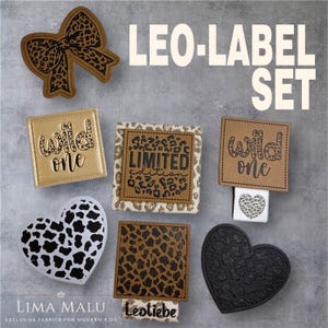 Könnte beinhalten: Eine Sammlung von Stoffetiketten und Verzierungen mit Leopardenmuster. Enthält eine Schleife, herzförmige und quadratische Etiketten mit den Worten "Wild One" und "Limited Edition". Der Text "Leo-Label Set" ist ebenfalls sichtbar.