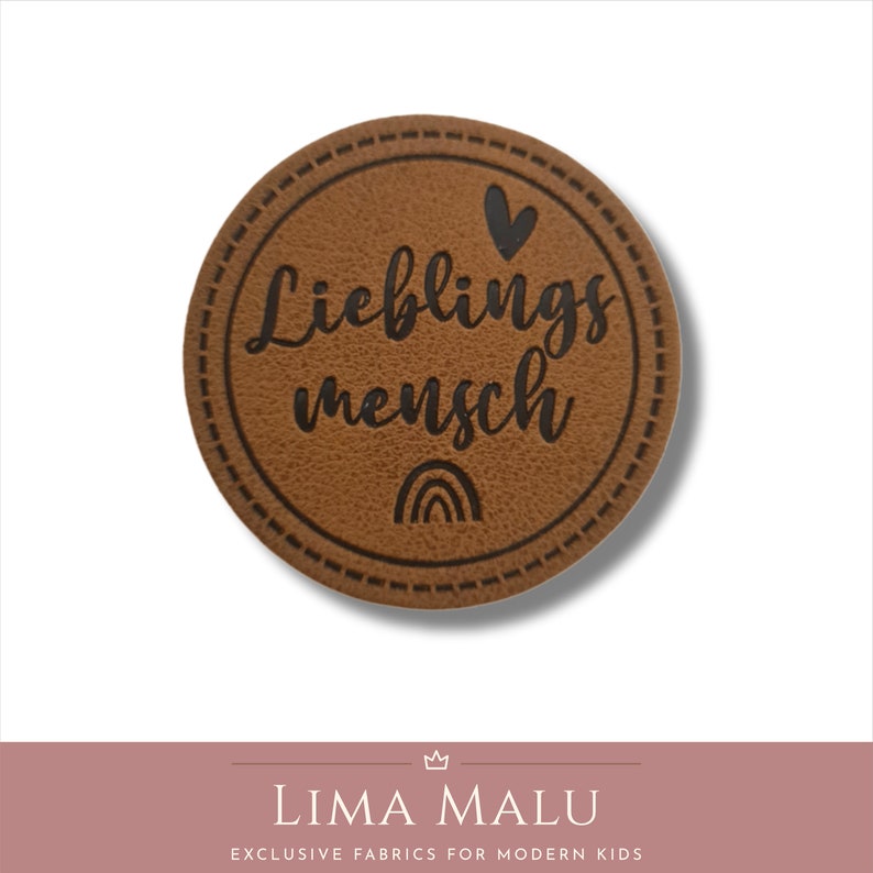 May include: Brown leather patch with a stitched border. The patch has a black heart, rainbow, and the text "Lieblingsmensch" in a cursive font.