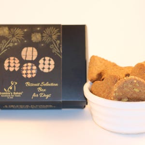May include: A black box with gold lettering that reads "Biscuit Selection Box for Dogs" and a small dog silhouette. The box is next to a white bowl filled with dog biscuits.