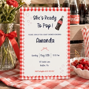 May include: Baby shower invitation with a red and white gingham border. The invitation reads "She's Ready To Pop!" and includes details for Amanda's baby shower, including the date, time, and location. A bottle of Coca-Cola is featured.