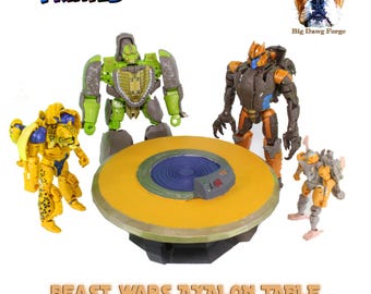 May include: A round yellow table with a central blue circular detail, surrounded by four articulated robot action figures in green, yellow, brown, and grey. The text MULTICOLOR PRINTED, Big Dawg Forge, and BEAST WARS AXALON TABLE appear in the image.