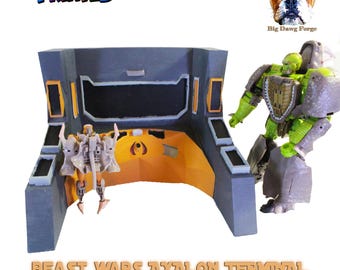 May include: A gray and orange plastic terminal console with a central screen area, accompanied by two action figures. One figure is small and light-colored, while the other is a larger green and gray robot. Text reads BEAST WARS AXALON TERMINAL.