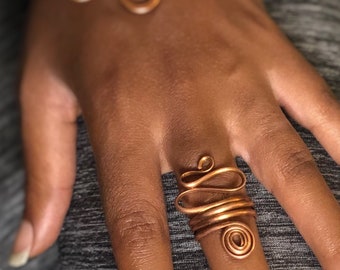 May include: A copper wire ring with a unique, abstract design. The ring is made of multiple coils of wire, creating a layered and textured look.