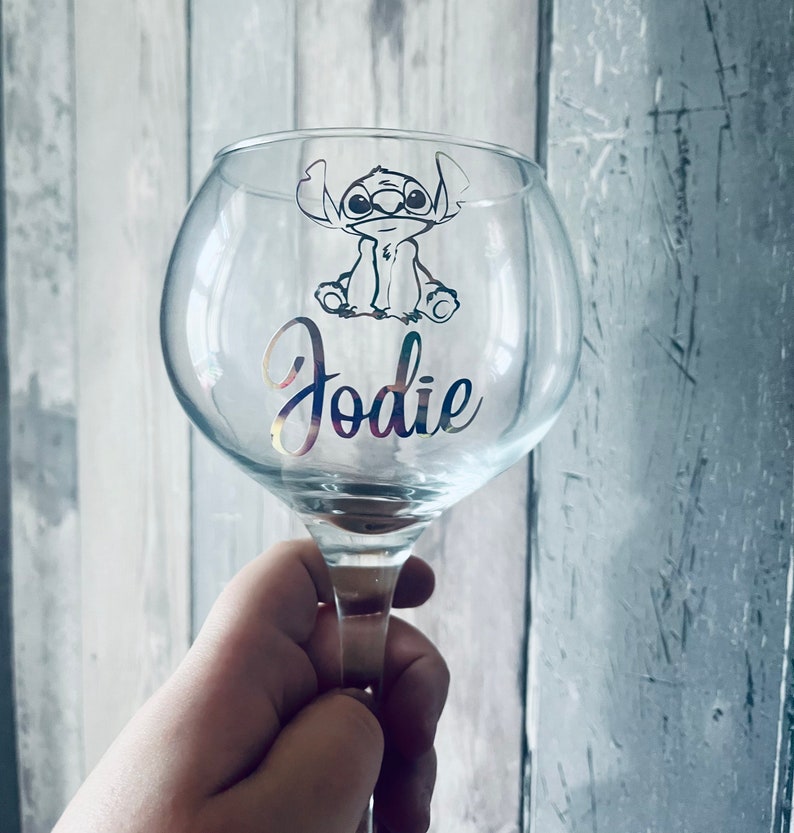 May include: A clear glass with a silver design of a cartoon character with the name "Jodie" on the glass.