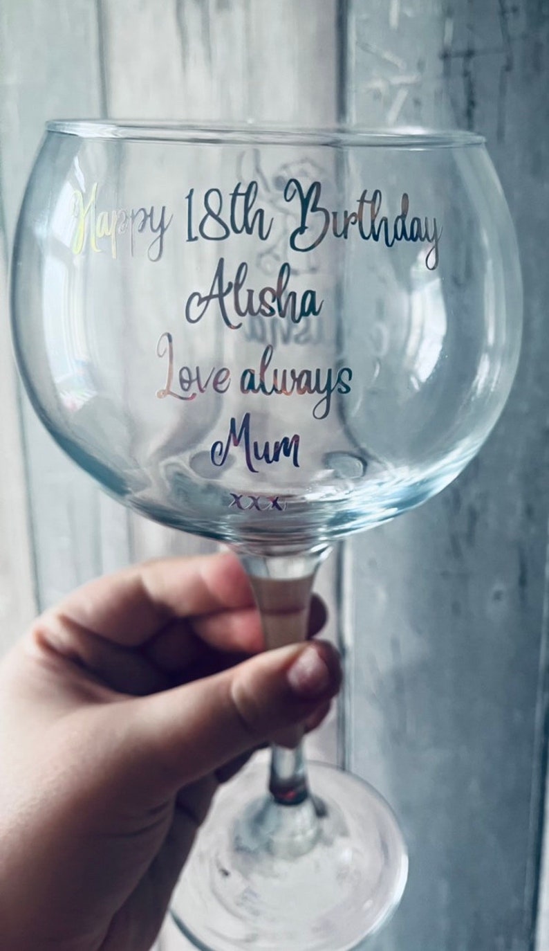 May include: A clear glass gin glass with a gold and silver inscription that reads "Happy 18th Birthday Alisha Love always Mum xxx".