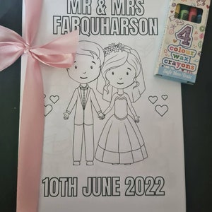 May include: A white coloring book with a pink ribbon and a box of crayons. The cover features a cartoon bride and groom with the text "MR & MRS FARQUHARSON" and "10TH JUNE 2022".