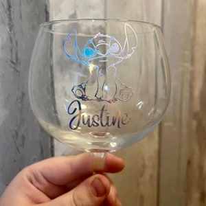 May include: A clear glass with a silver design of Stitch from Lilo & Stitch. The glass has the name Justine written on it.