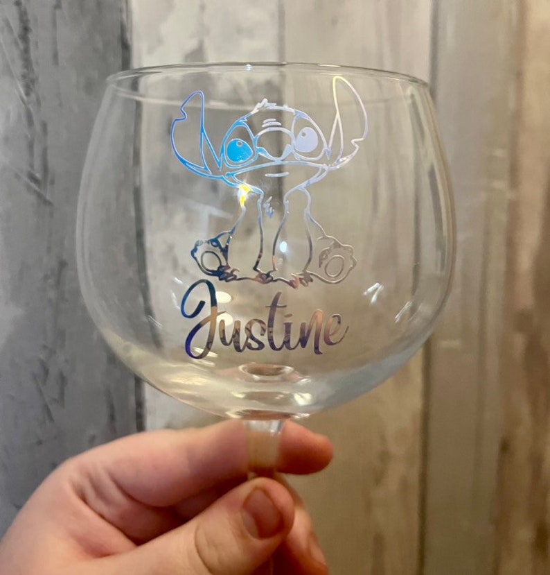 May include: A clear glass with a silver design of Stitch from Lilo & Stitch. The glass has the name Justine written on it.