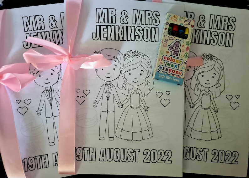 May include: Two coloring book pages with a bride and groom, a pink ribbon, and a box of four color wax crayons. The pages say "Mr. & Mrs. Jenkinson" and "19th August 2022".