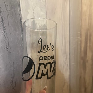 Puede incluir: Un vaso de vidrio transparente con un logotipo de Pepsi negro y el texto "Lee's Pepsi" en &eacute;l.